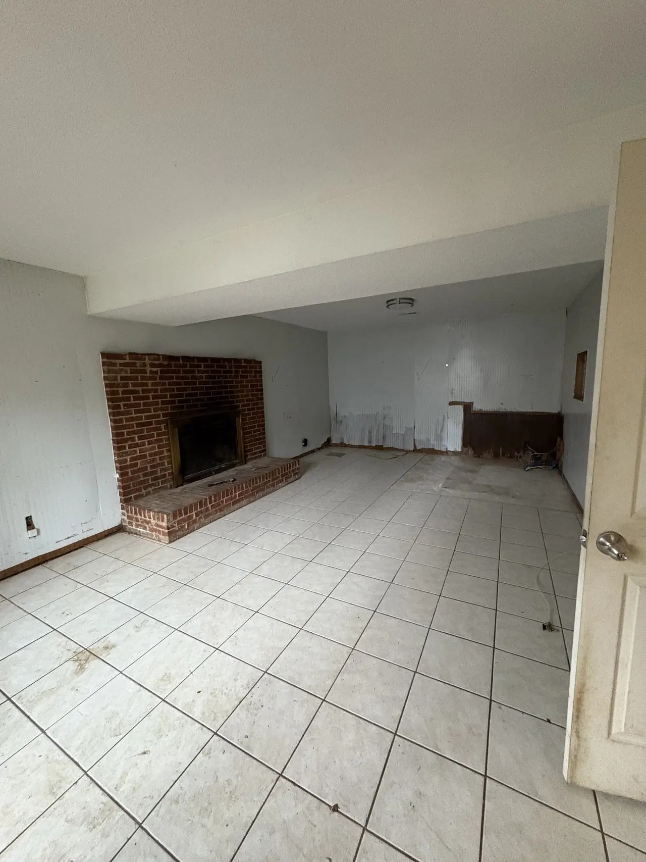 Basement family room before renovation, with a brick fireplace, white tile flooring, and stripped paneling