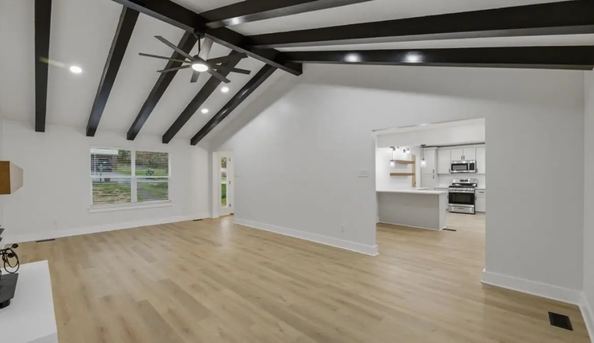Living room with dark ceiling beams, open to the kitchen through a wide doorway, with light wood-look plank flooring