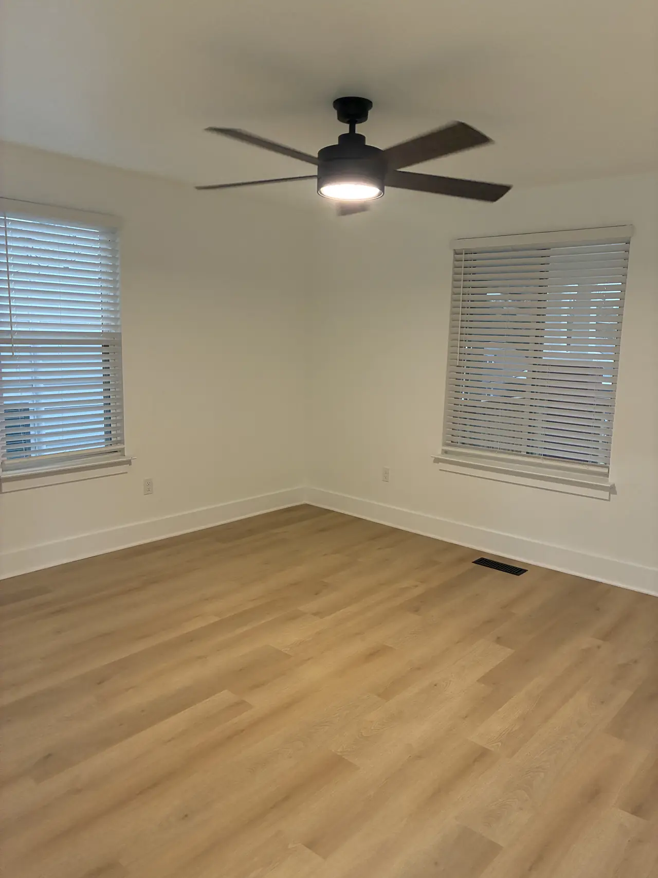 Bedroom with two windows, white blinds, a black ceiling fan, and light wood-look plank flooring
