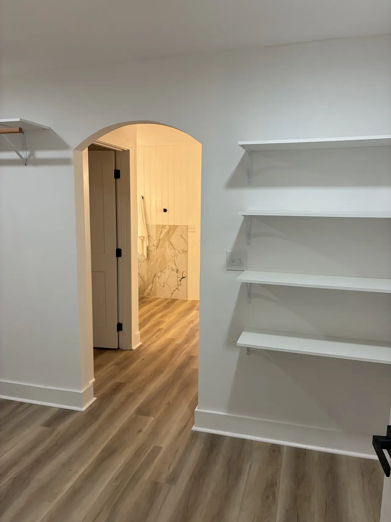 Walk-in closet with white wall shelves and a hanging rod, and an arched doorway