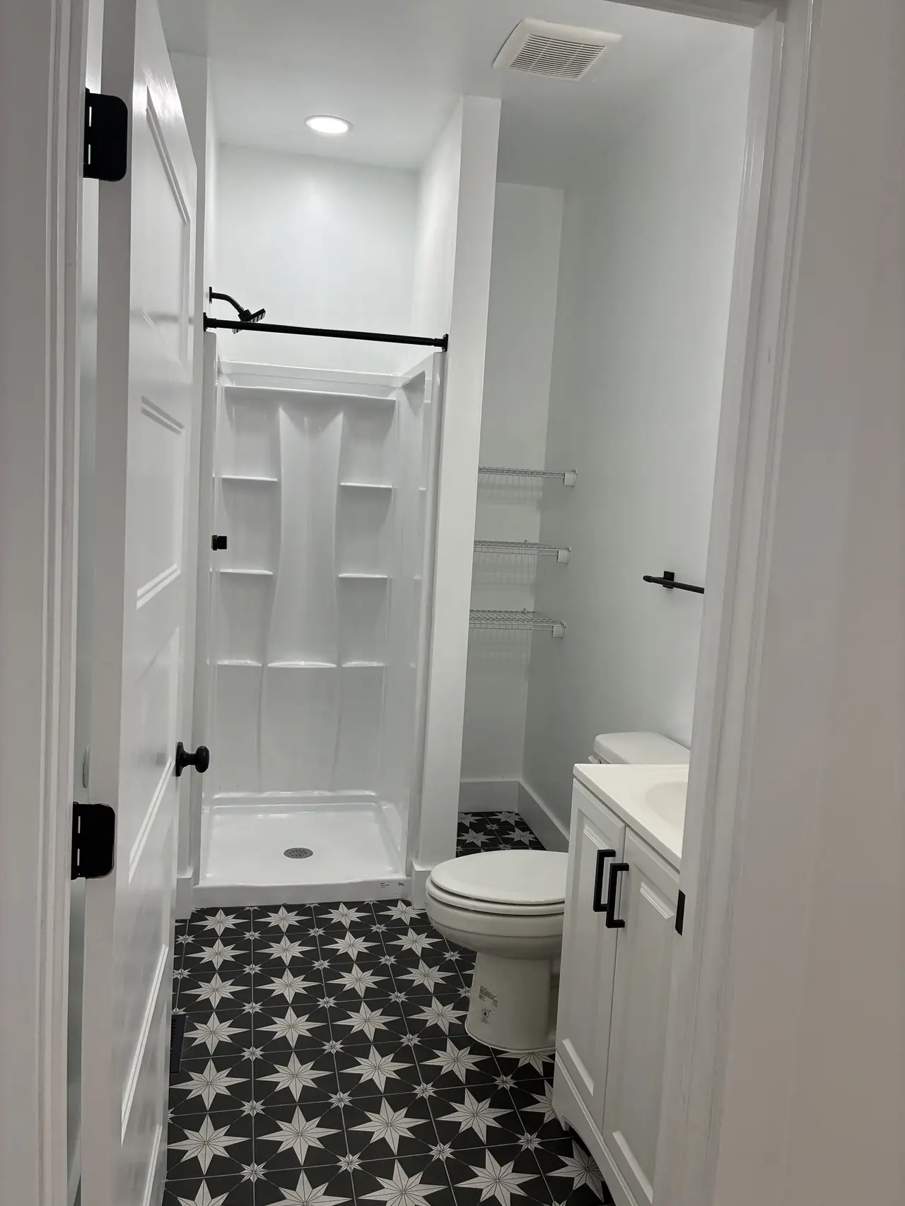 Renovated bath with a white one-piece shower stall, a black-and-white star-pattern tile floor, and a white vanity with black hardware