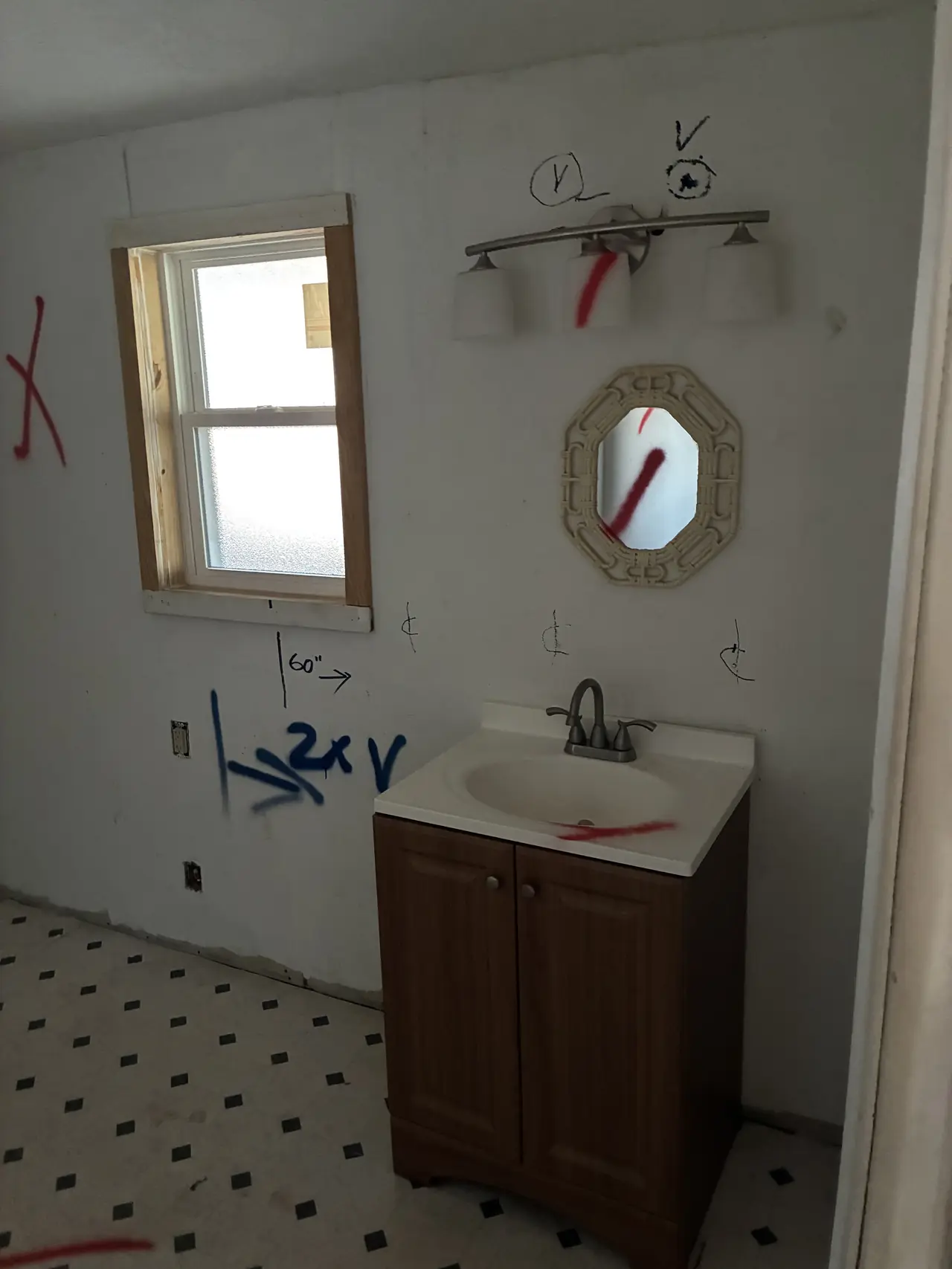 Hall bath before renovation: a small wood vanity, an old light bar, black-dot vinyl flooring, and demolition marks on the walls