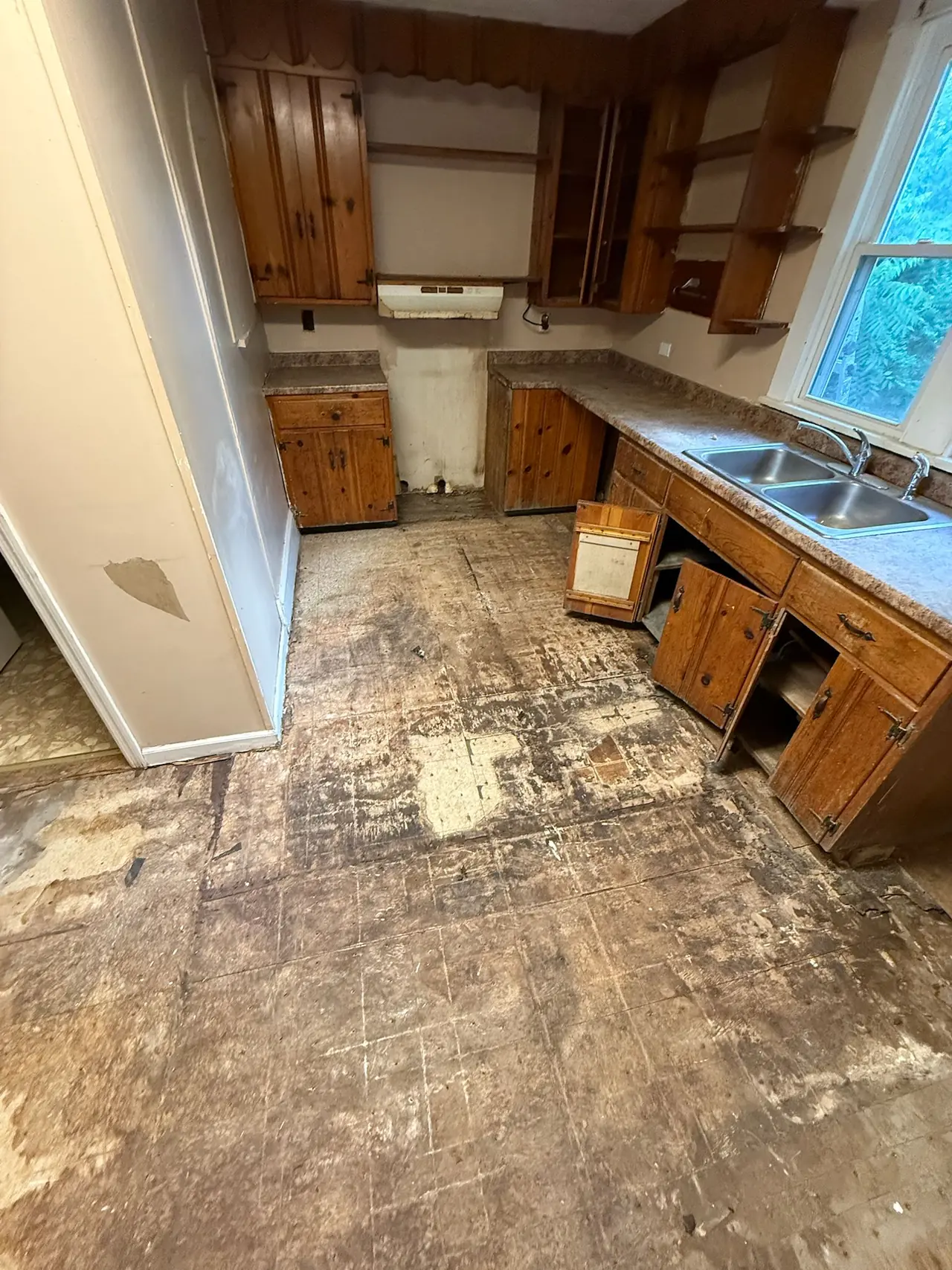 Kitchen before renovation, with dated wood cabinets and the old flooring torn out