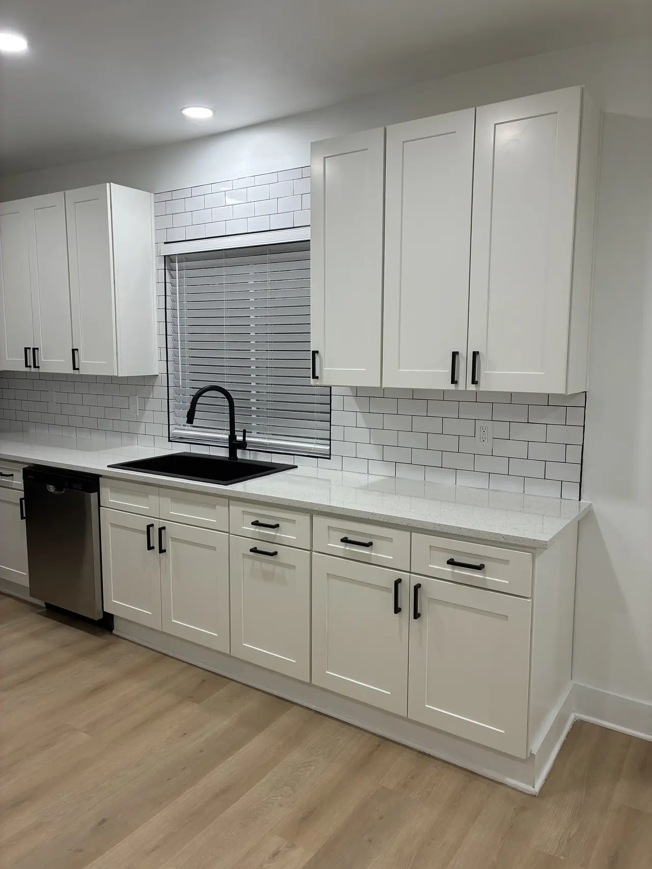 Kitchen sink wall with white subway tile, white shaker cabinets, and a black sink
