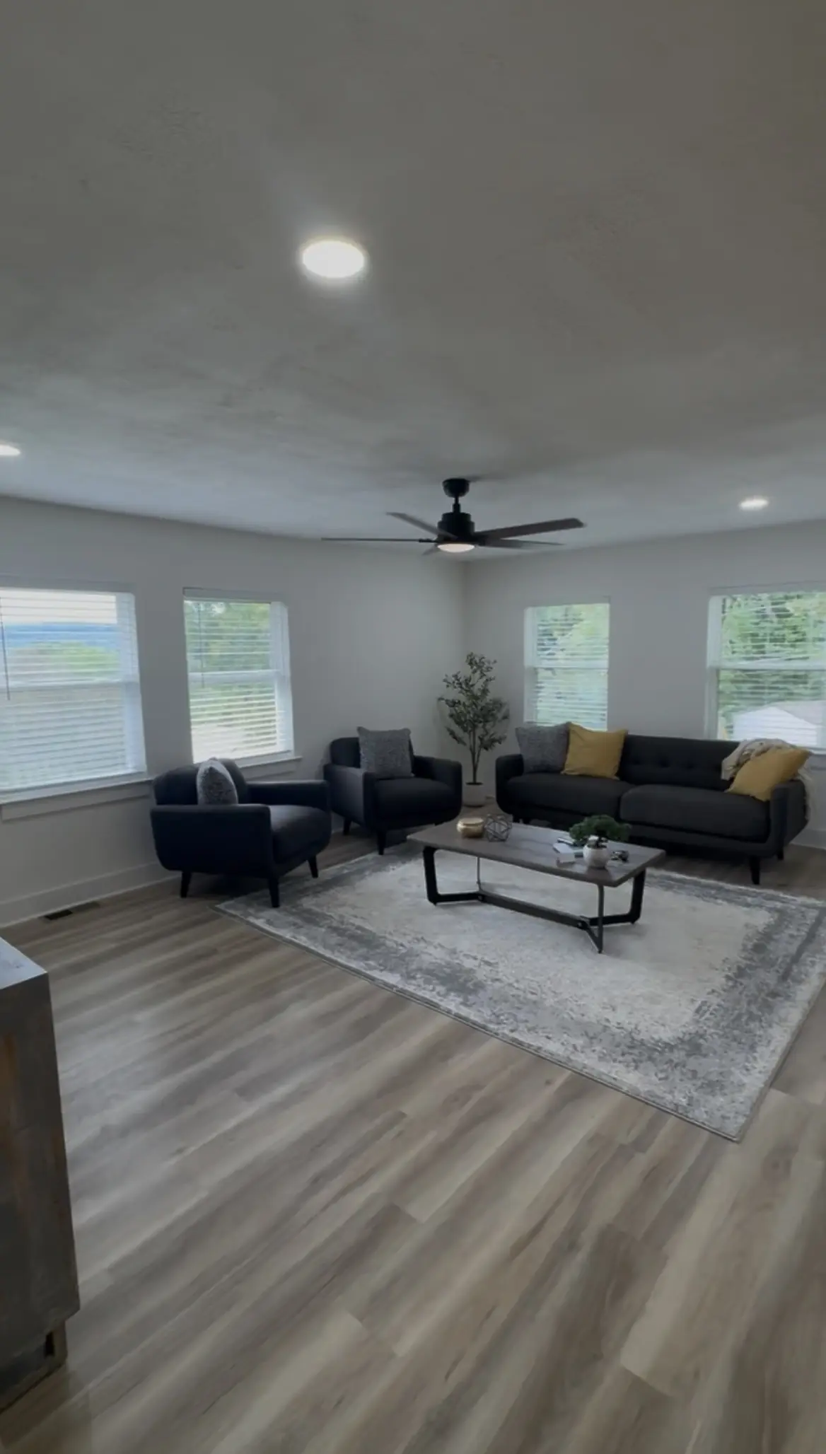 Renovated living room with white walls, new window blinds, recessed lights, a black ceiling fan, and wood-look plank flooring