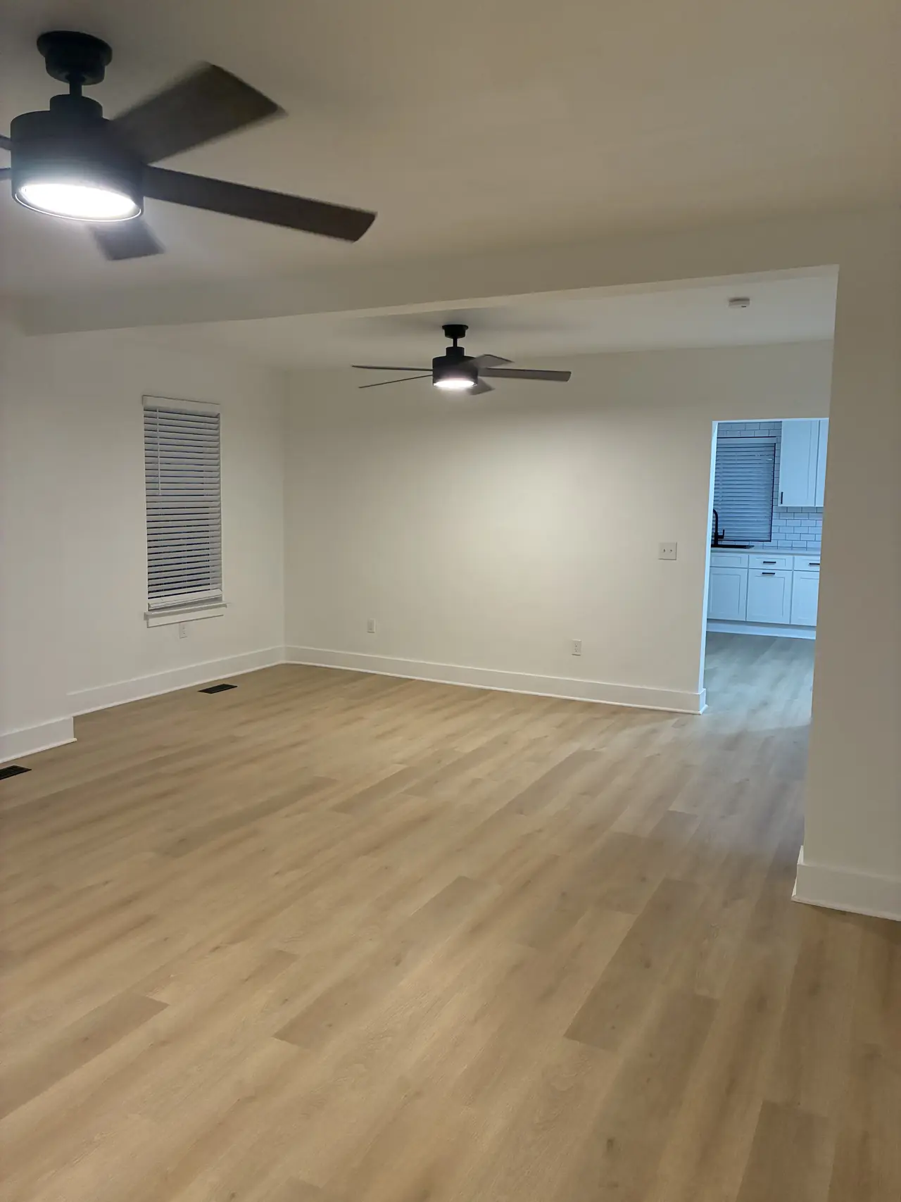 Open living room with two black ceiling fans and a doorway into the white kitchen