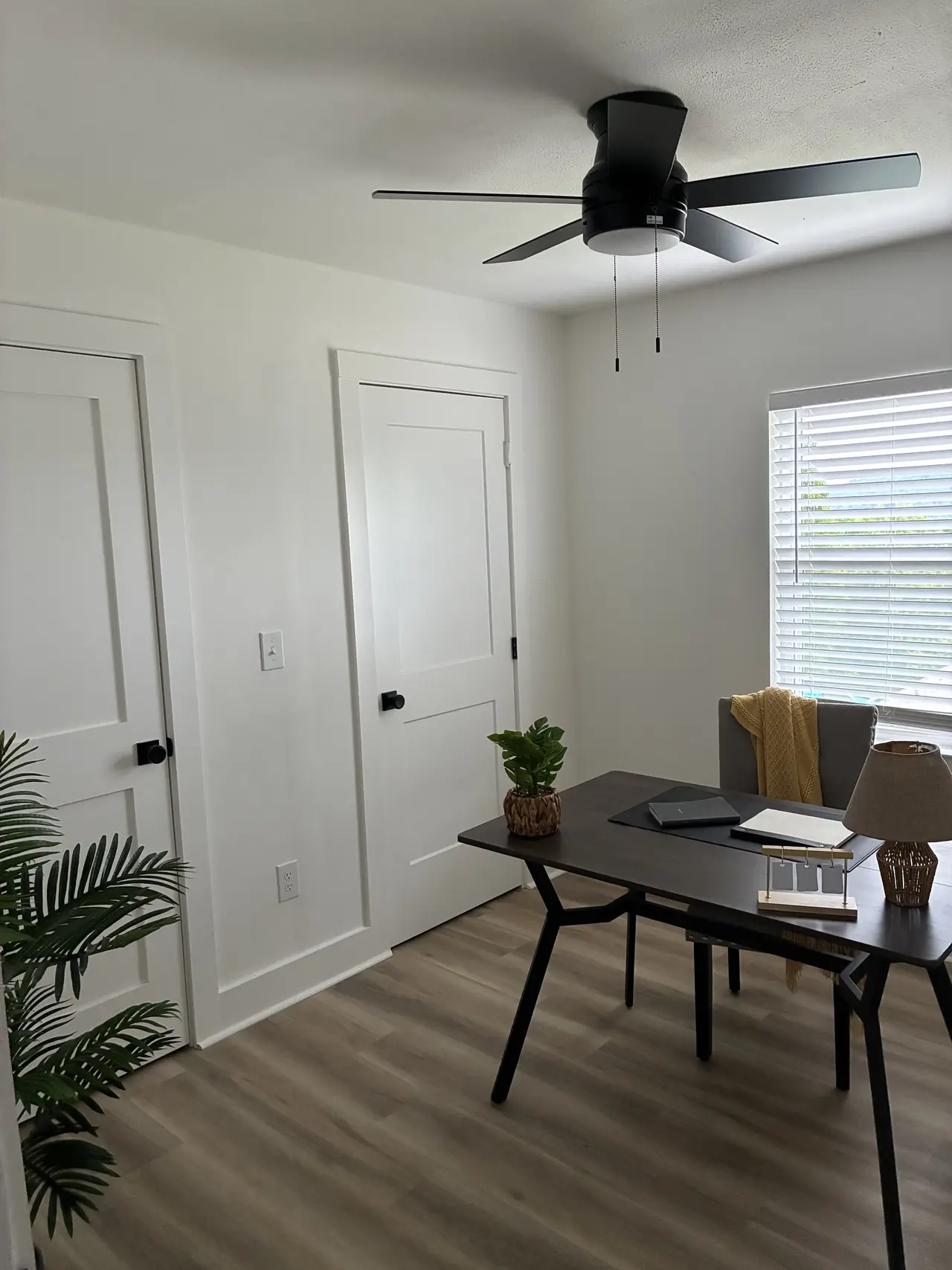 Bedroom set up as an office, with white two-panel doors, black hardware, a black ceiling fan, and wood-look plank flooring