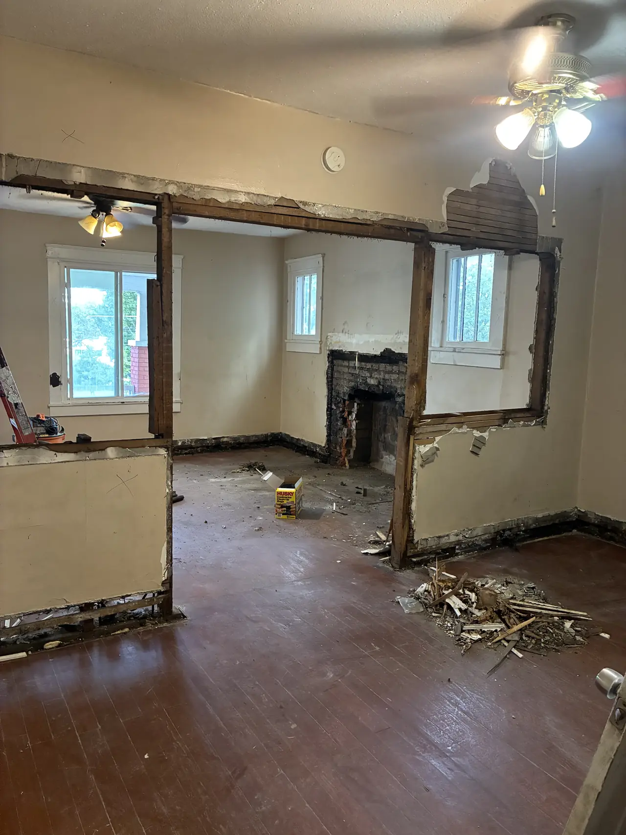 Living room during demolition: a partition wall opened to its framing, with an old brick fireplace in the room beyond