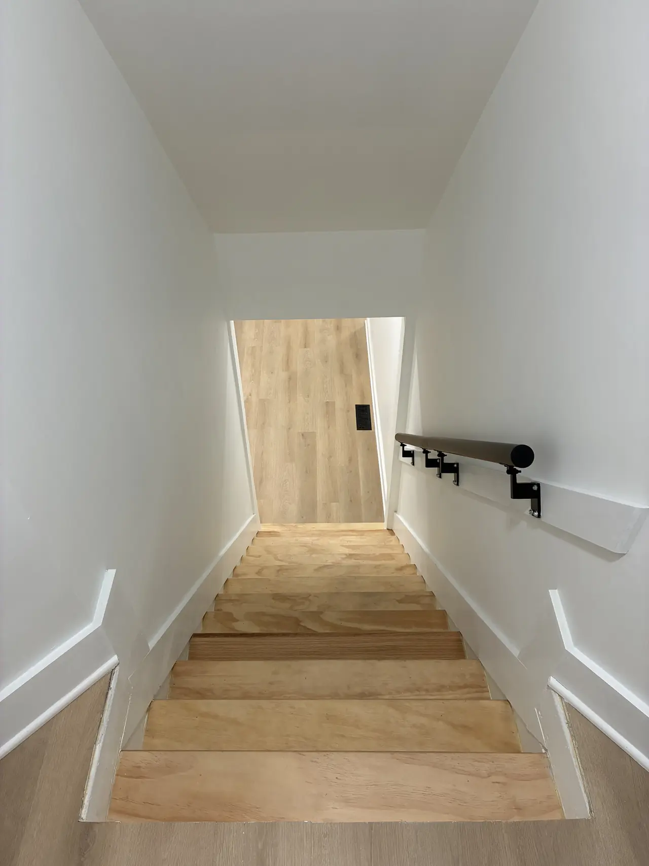 Staircase with new wood treads, white walls, and a wooden handrail on black brackets